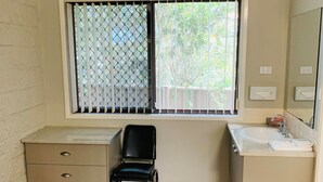 Une salle de bain avec une fenêtre, un lavabo, un miroir, une chaise et un meuble.