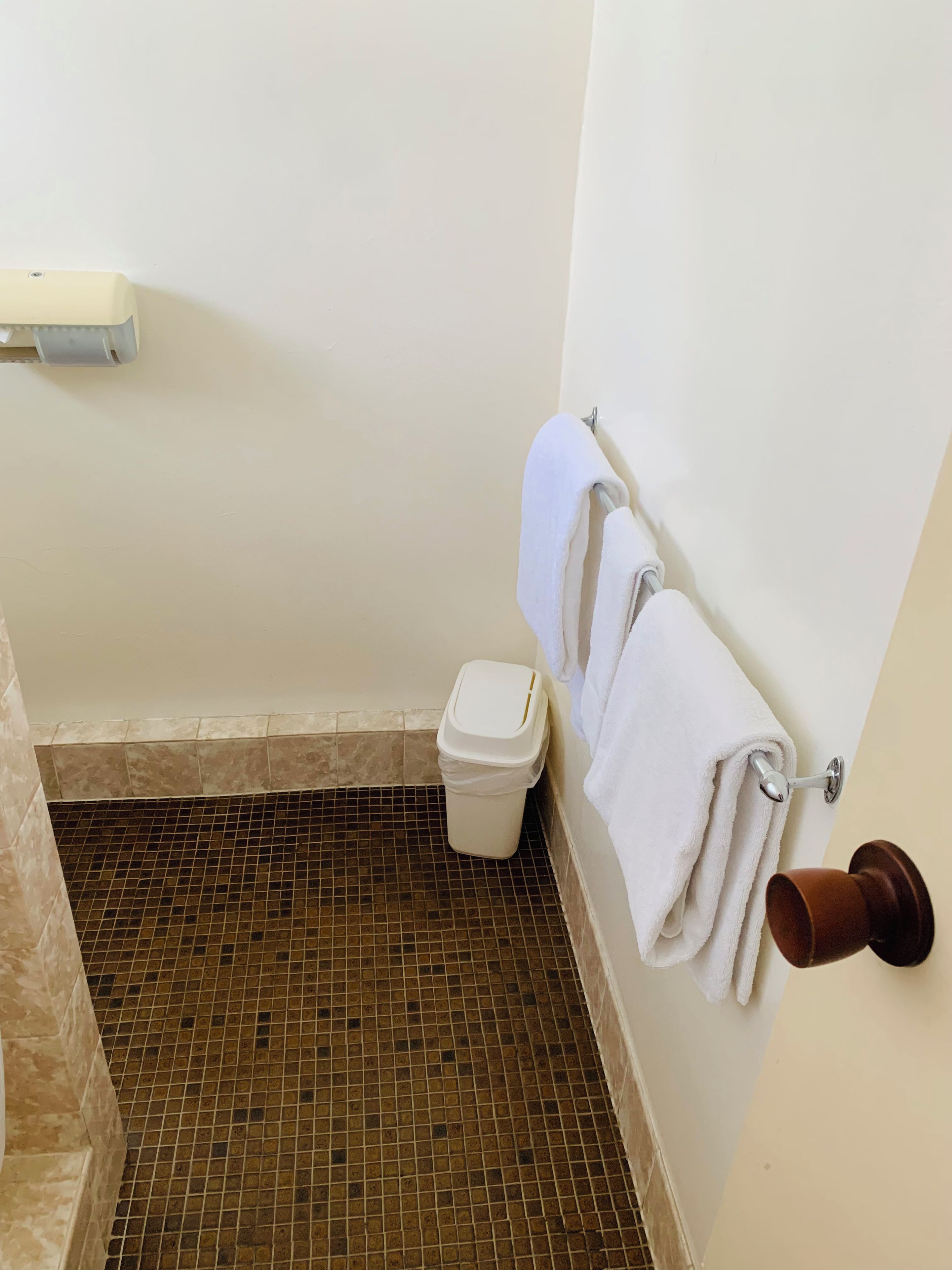 A bathroom with a tiled floor, a white toilet, a trash bin, and a towel rack with a white towel.