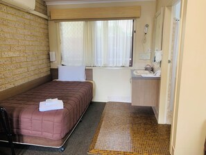 Una habitación de hotel pequeña y funcional con una cama individual, ventana con cortinas, lavamanos y espejo.