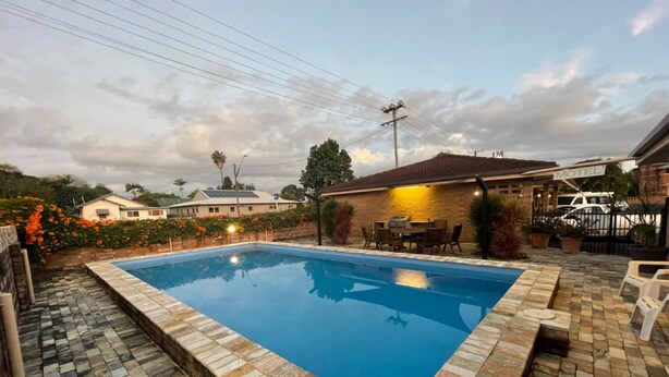 A rectangular swimming pool with a tiled edge, surrounded by a patio area with stone tiles. - Milgate Motel (Casino)