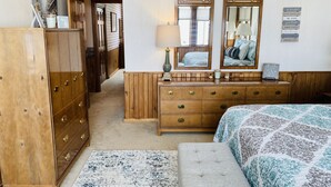 A hotel room with a wooden dresser, a bed with a patterned bedspread, a mirror with decorative frames, and a wall with inspirational quotes.