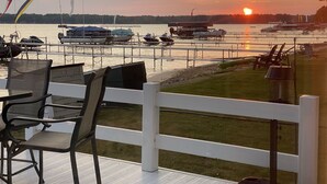 A waterfront restaurant with outdoor seating, a view of the sunset over the water, and boats docked nearby.
