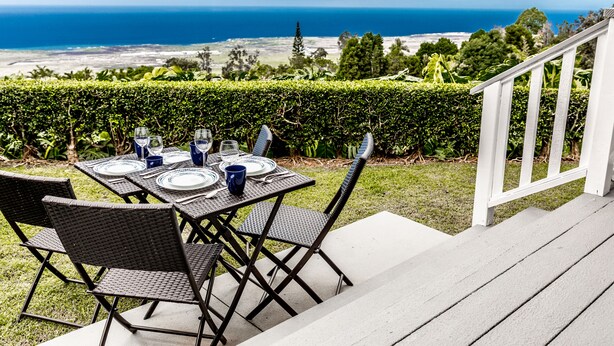 An outdoor dining area with a table set for four, overlooking a scenic view of the ocean and distant land.