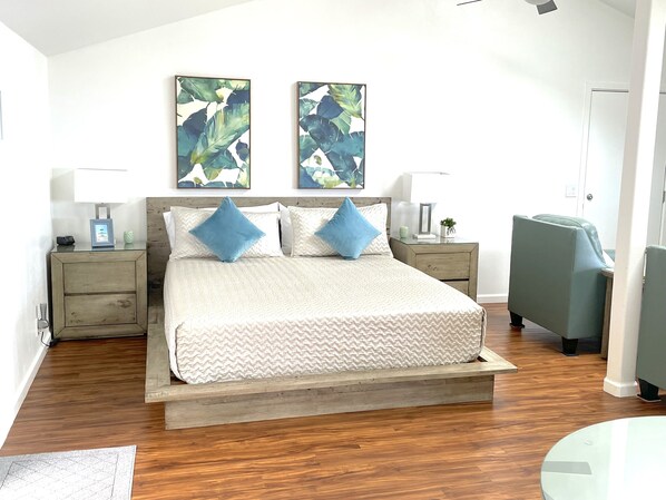 A bedroom with a bed, two nightstands, a chair, and artwork on the wall.