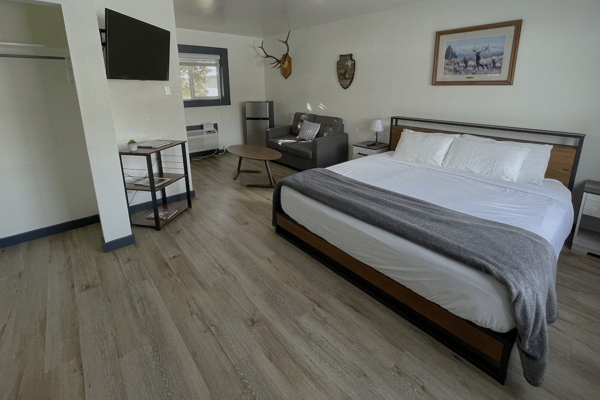 A modern bedroom with a large bed, a grey sofa, a small table, and a wall-mounted TV.