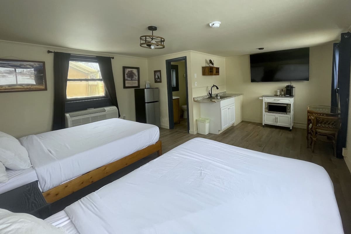 A hotel room with two beds, a kitchenette, a TV, and a window with curtains.