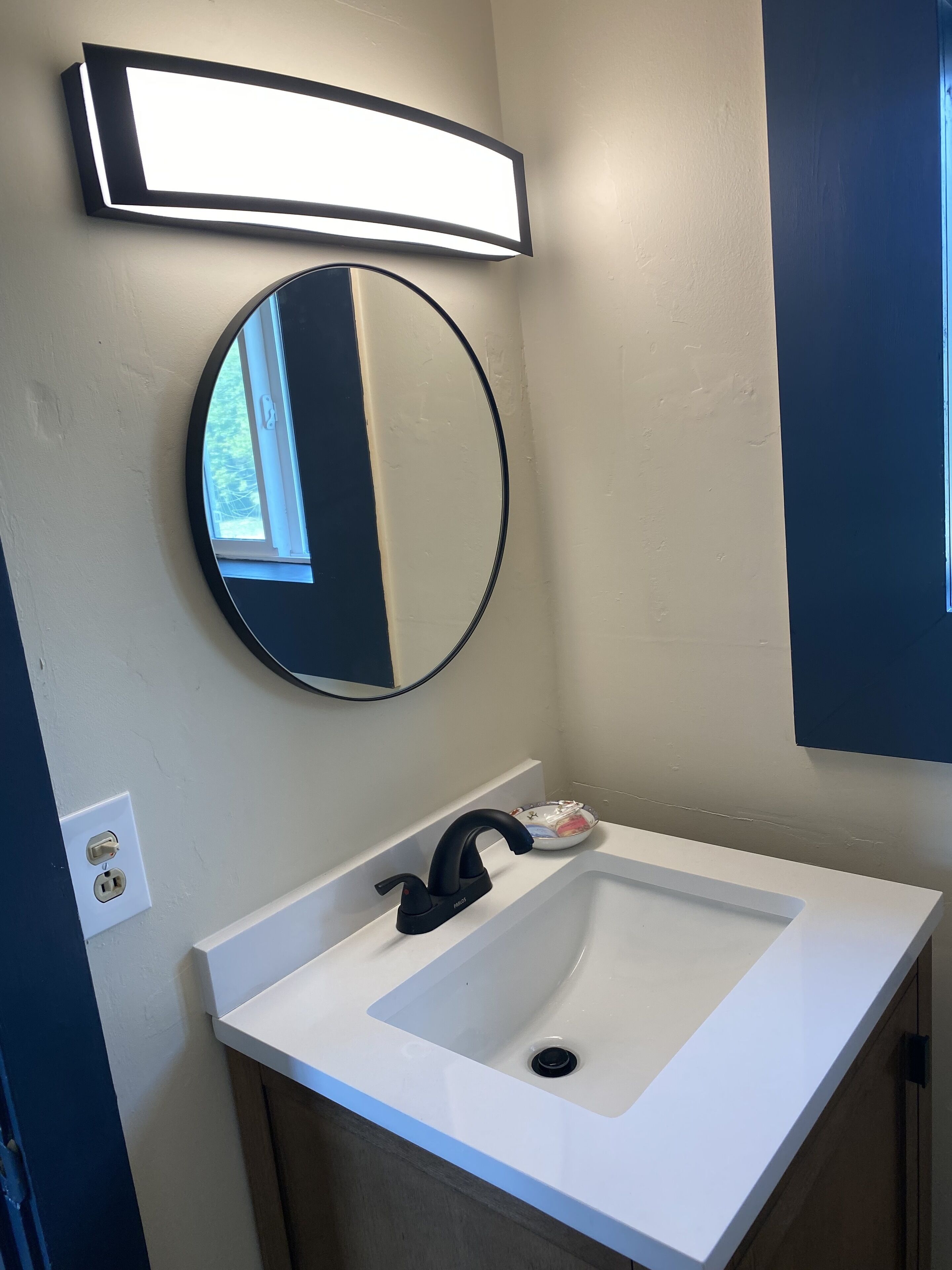 A bathroom with a white sink, black faucet, and a round mirror.