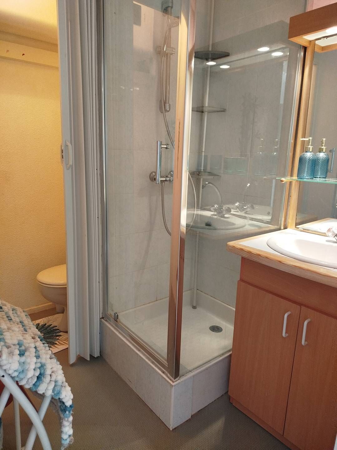 Et moderne badeværelse med en glasvæg omkring bruseniche, et trækommode med vask og et toilet.