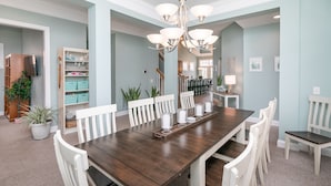 Un comedor con una larga mesa de madera, sillas blancas y un candelabro.