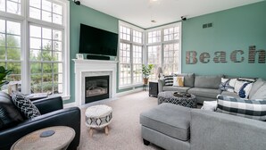 Un salón con chimenea, ventanas amplias y una decoración mural con la palabra 'Beach'.