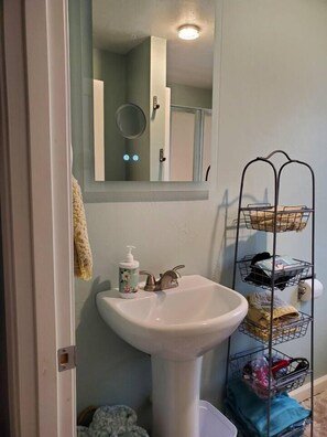 Une salle de bain avec un lavabo blanc, un miroir et un étagère en métal avec des paniers.