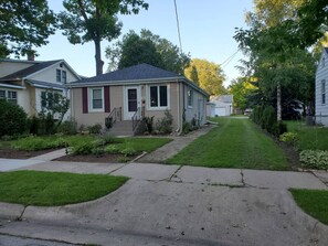 Une maison de plain-pied avec un porche à l’avant, un petit jardin devant et une allée menant à la porte d’entrée.