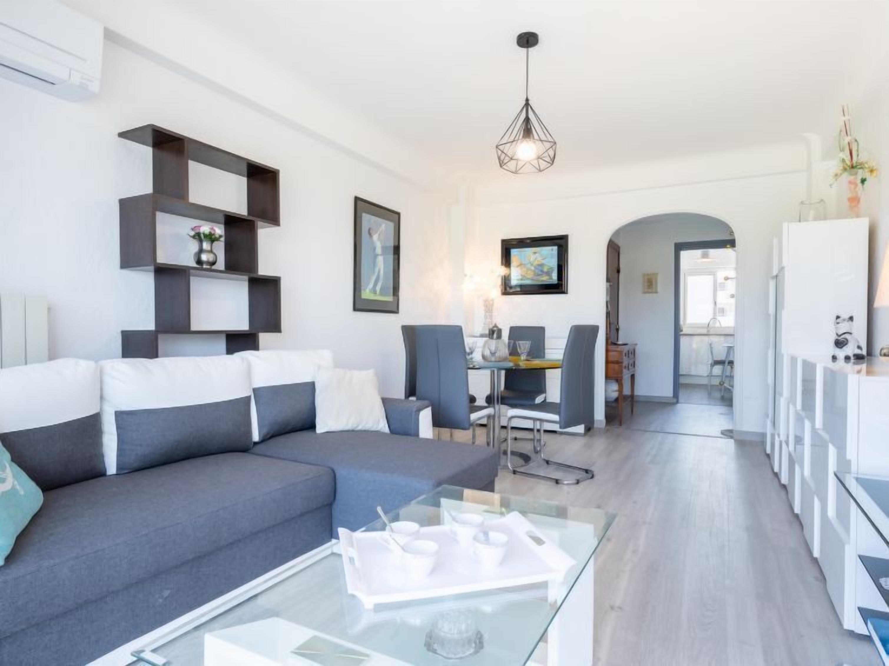 Una sala de estar moderna con un sofá gris, una mesa de centro de vidrio y una zona de comedor con sillas y una mesa.