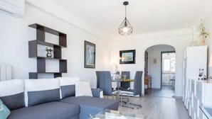 Una sala de estar moderna con un sofá gris, una mesa de centro de vidrio y una zona de comedor con sillas y una mesa.