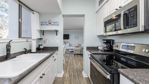 Una cocina moderna con armarios blancos, encimeras de granito y electrodomésticos de acero inoxidable, incluyendo una placa de cocina y un microondas.