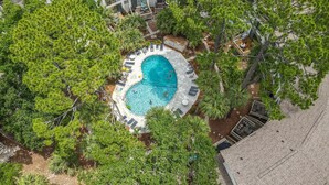 Vista aérea de un resort con una piscina circular rodeada de sillones de descanso y una terraza.