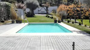 A swimming pool with a paved deck, surrounded by a grassy area and trees. - House (Póvoa de Lanhoso)