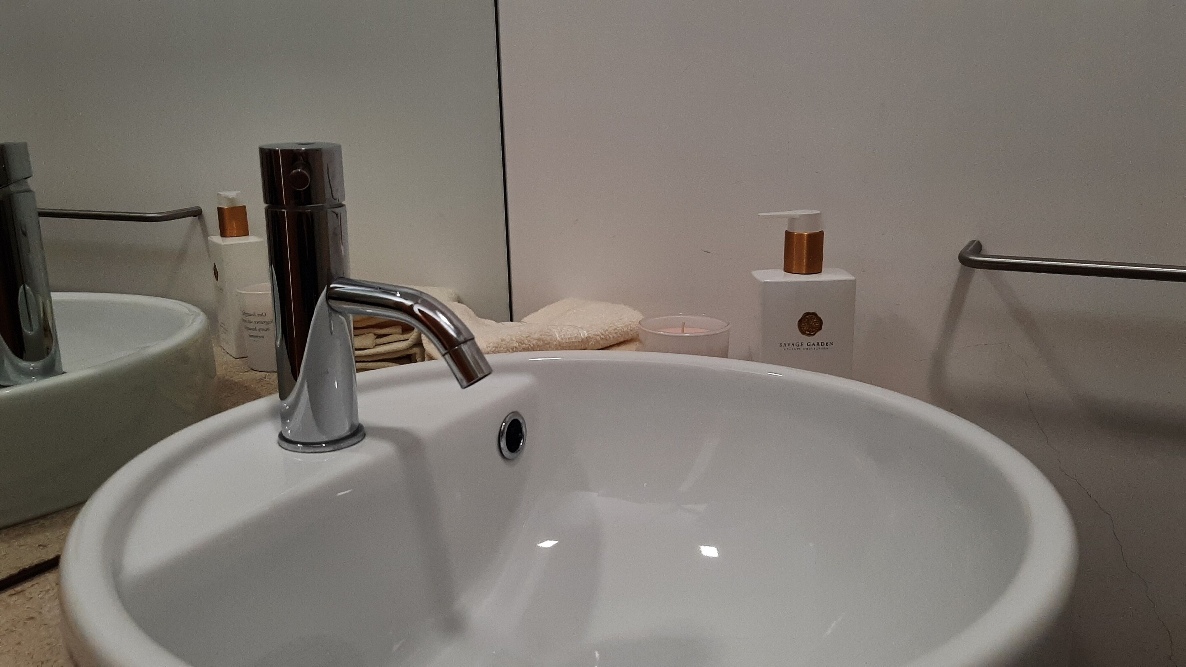 A bathroom with a white sink, a chrome faucet, a towel rack, and a bottle of soap.
