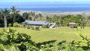 A house with a large roof, surrounded by lush greenery and a view of the ocean. - Private Peaceful Beautiful House  (Kailua-Kona)