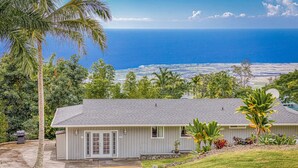 A single-story house with a grey roof and white siding, surrounded by lush greenery and a view of the ocean. - Private Peaceful Beautiful House  (Kailua-Kona)