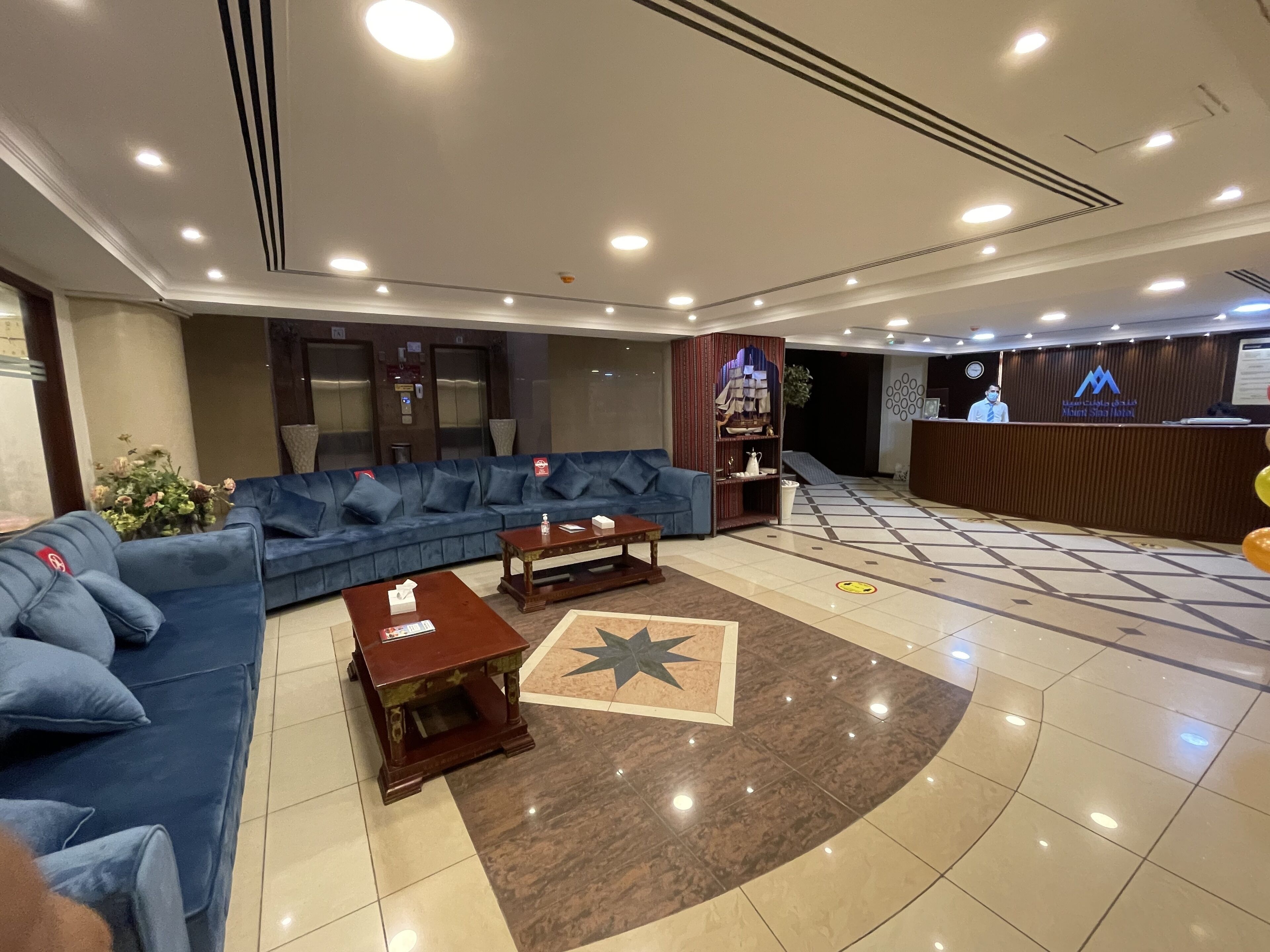 A hotel lobby with a blue sofa set, a reception desk, and a star-patterned rug.