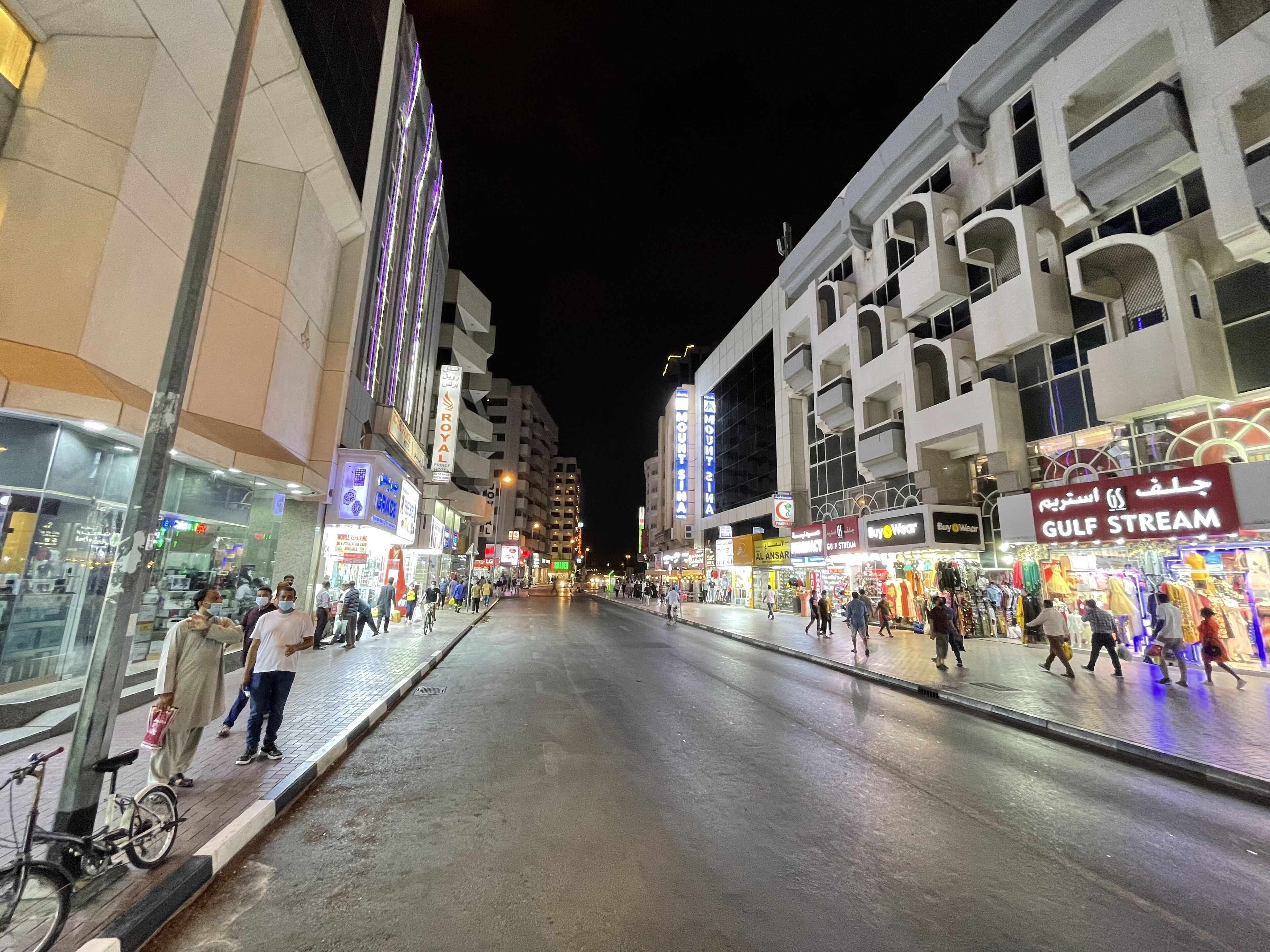 A nighttime street scene with modern buildings, shops, and pedestrians.
