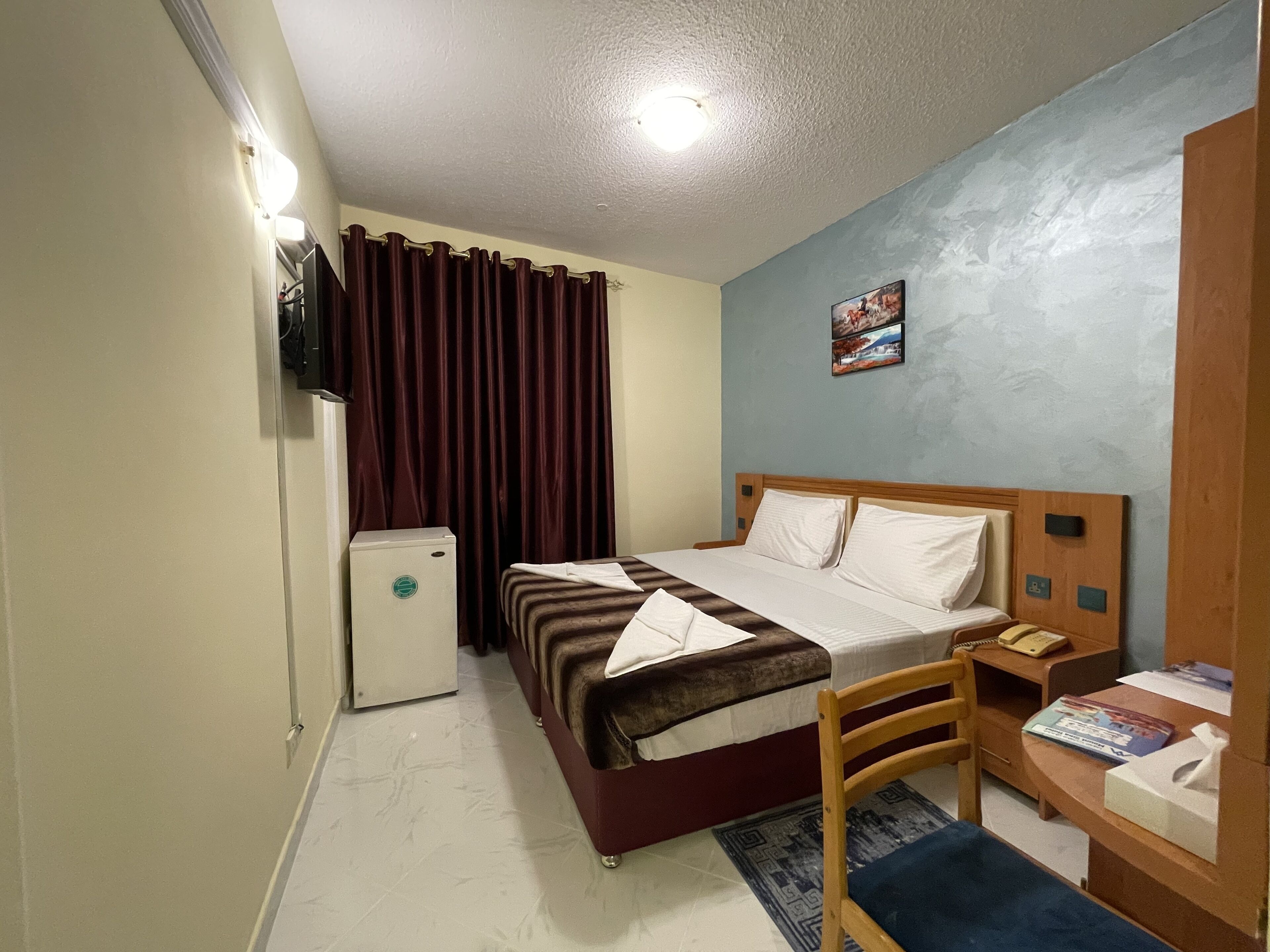 Hotelkamer met een bed, een bureau met stoel, een kleine verwarming en een televisie aan de muur.