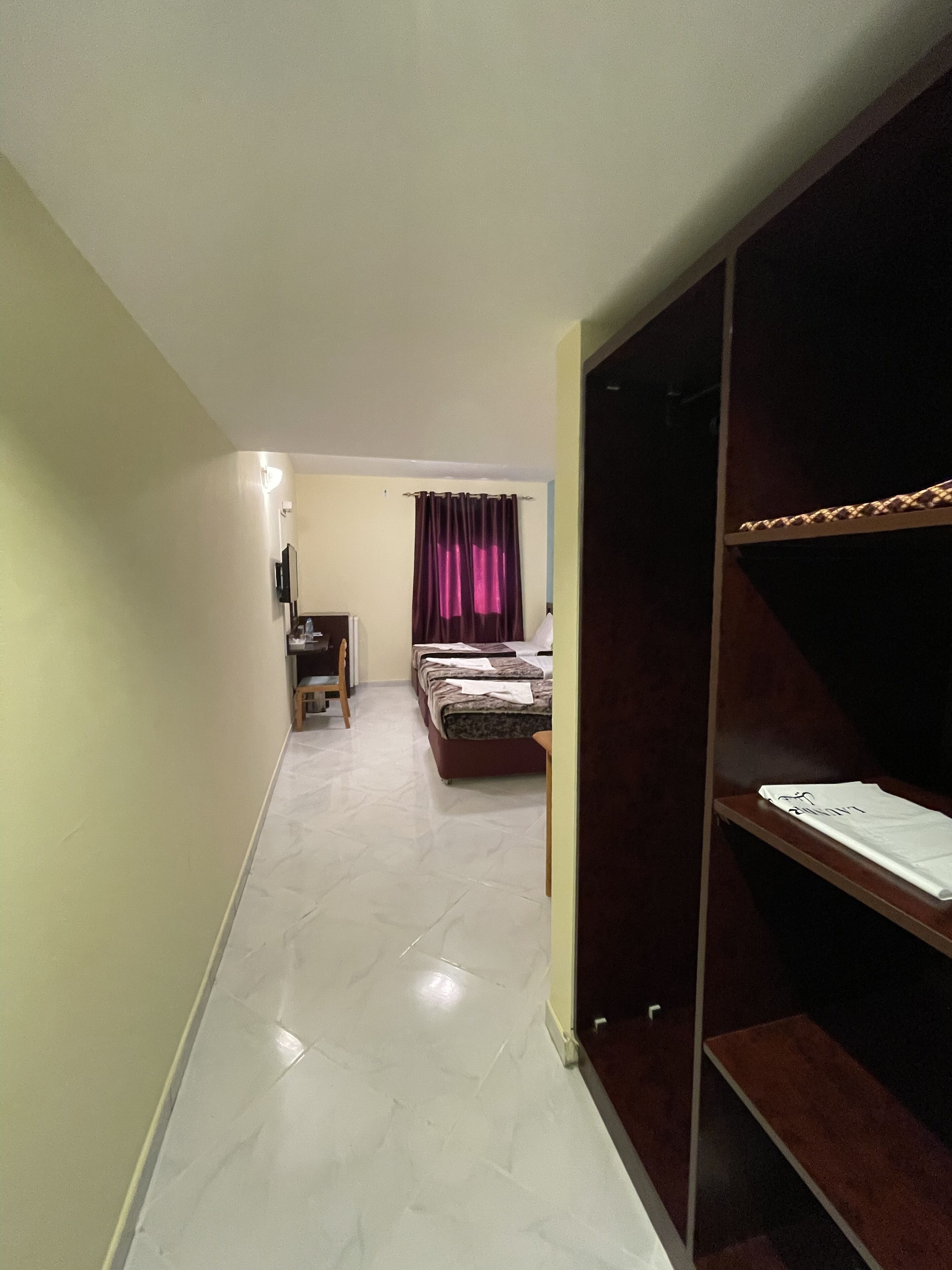 A narrow hallway leading to a bedroom with a bed, a desk, and a chair.