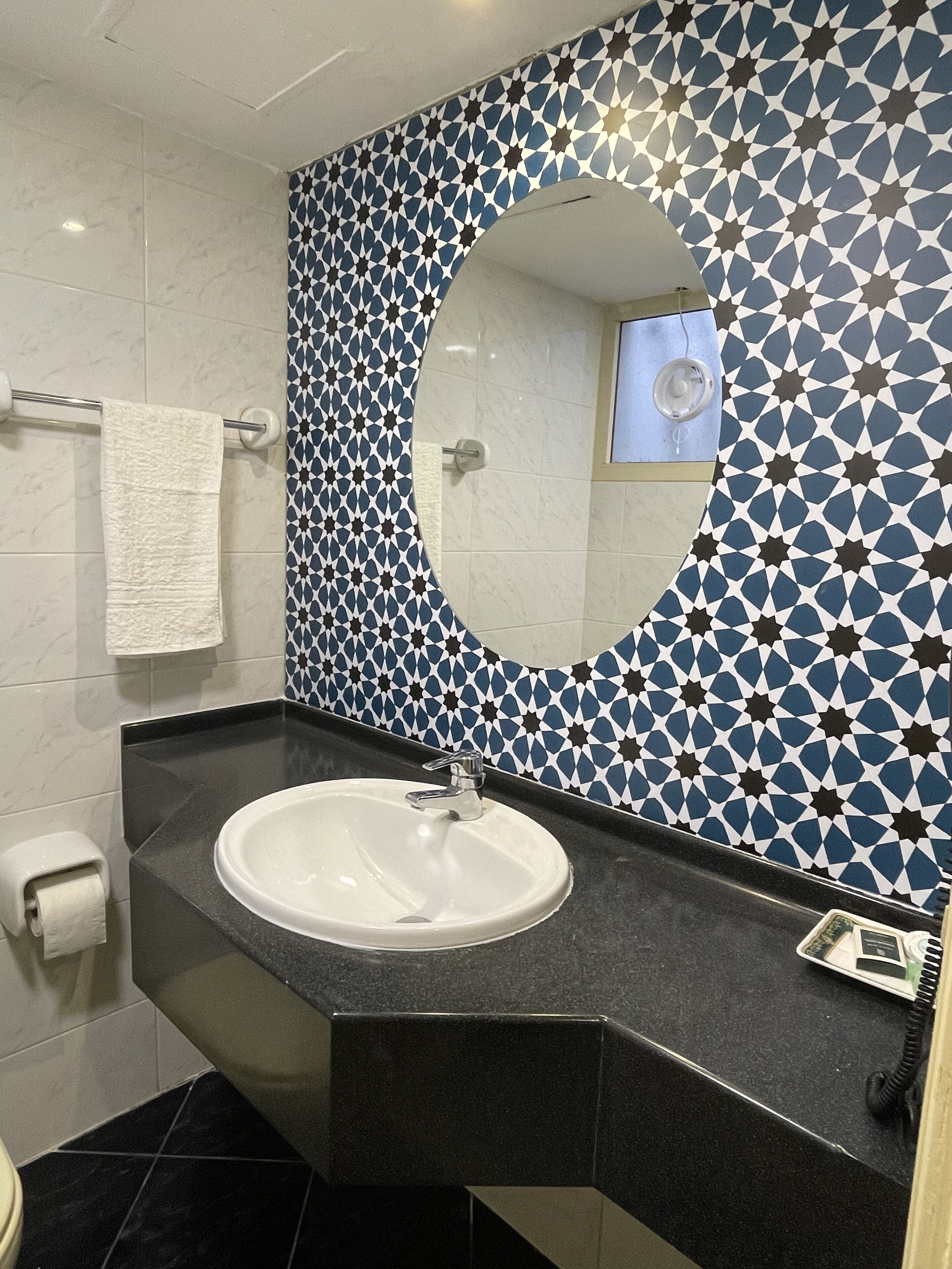 A bathroom with a white sink, a mirror, and a patterned tile wall.
