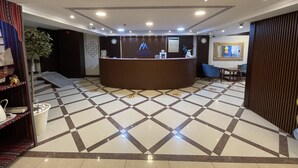 A reception area with a check-in counter, a clock, and a framed artwork on the wall. - MOUNT SINA HOTEL BY AURA (Dubai)