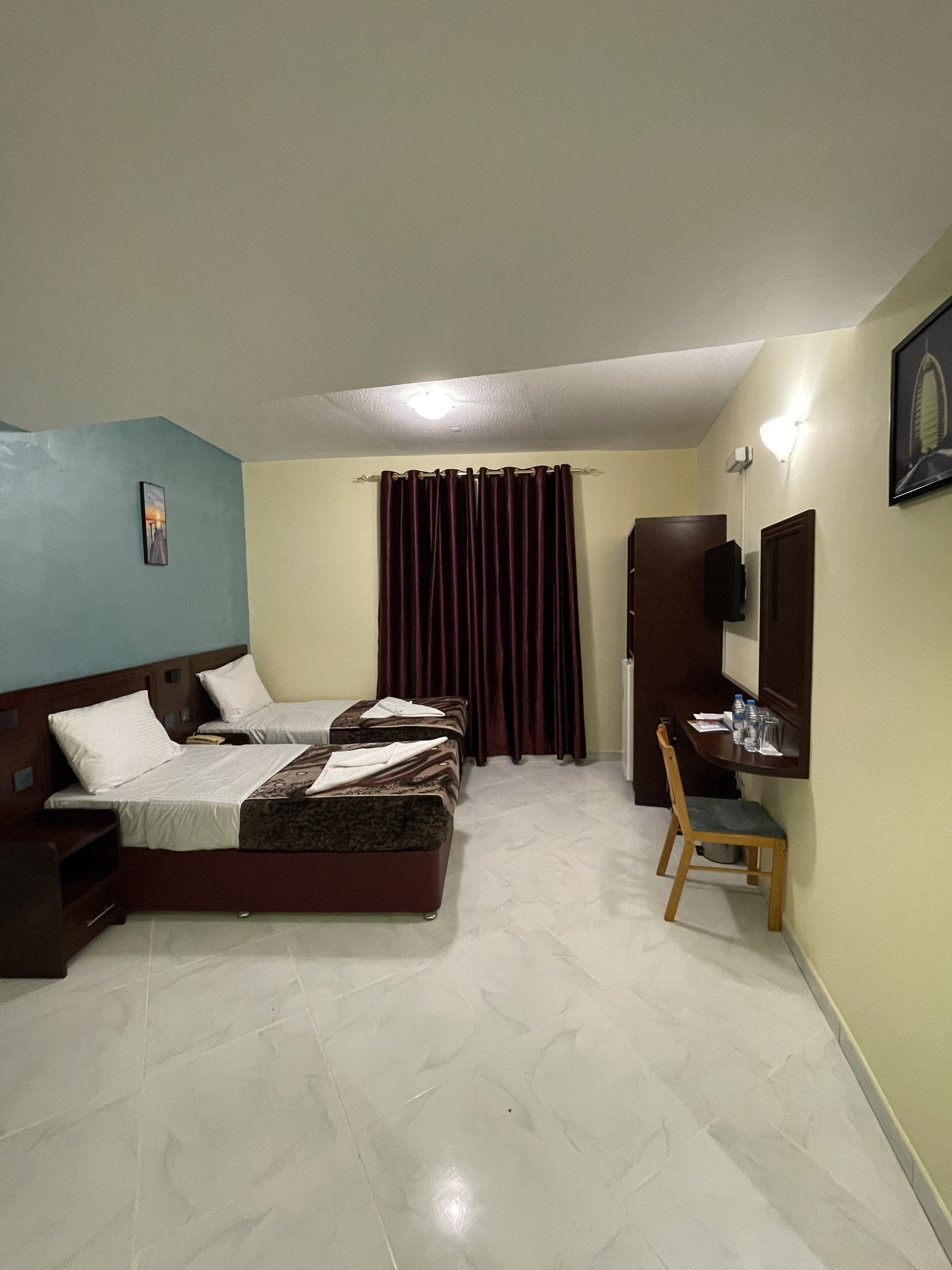Habitación de hotel con dos camas, un escritorio, una silla, un televisor y una cortina.