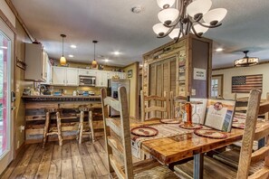 A rustic kitchen with wooden bar stools, a wooden dining table, and a chandelier.