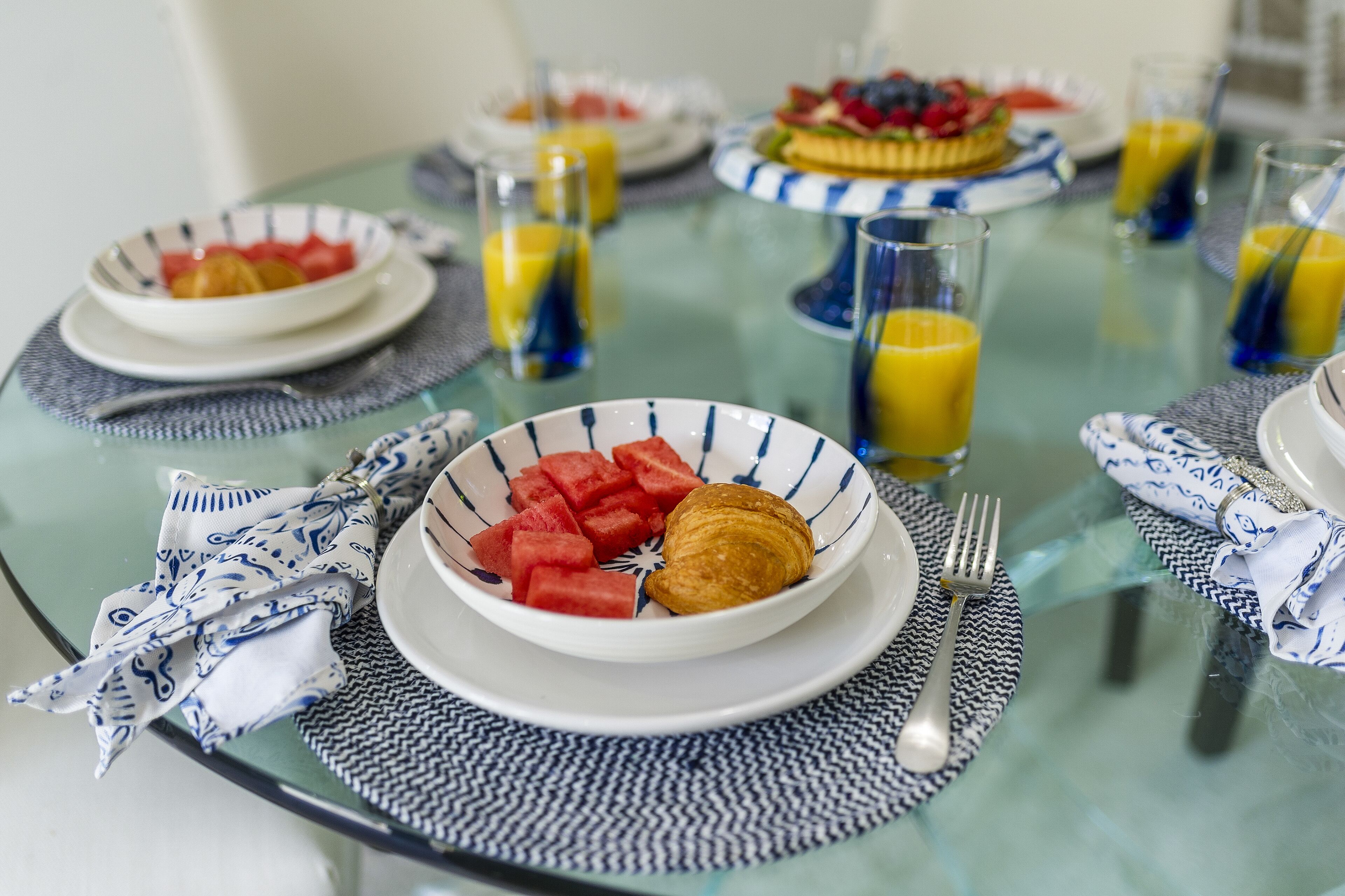 Une table mise pour le petit-déjeuner, avec une table en verre, des assiettes remplies de nourriture et des verres de jus d’orange.