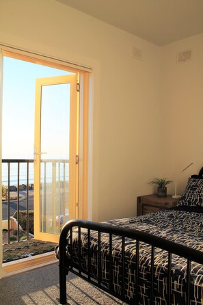A bedroom with a bed, a nightstand, a potted plant, and a view through a sliding glass door.
