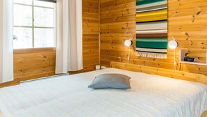 Una habitación de cabaña de madera con una cama, una ventana con cortinas, una lámpara fijada a la pared y un reloj digital.