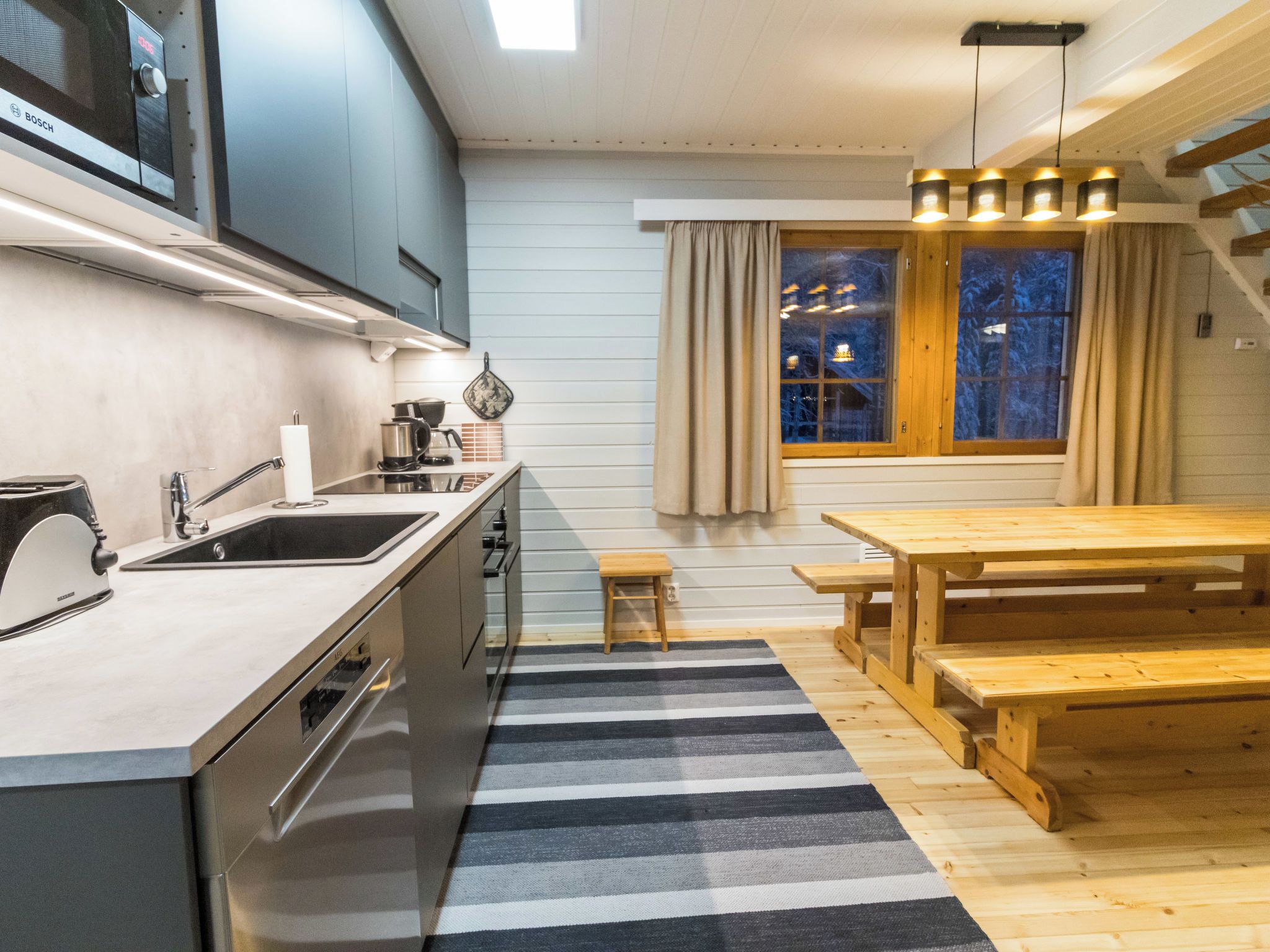 A modern kitchen with a built-in Bosch microwave, a wooden dining table, and a striped rug.
