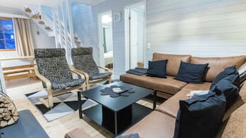 A modern living room with a sofa, two patterned armchairs, a coffee table, and a staircase leading to an upper level.