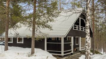 A cabin with a sloped roof, surrounded by trees and covered in snow.