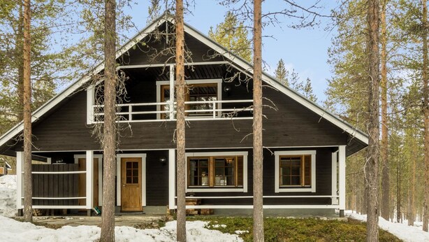 Una cabaña de dos pisos con fachada de madera oscura, detalles blancos y ventanas grandes.