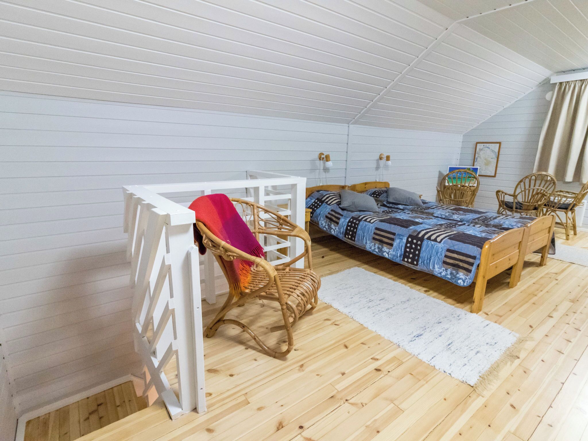 A cozy attic bedroom with a wooden bed, a white desk, and wicker chairs.