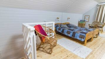 A cozy attic bedroom with a wooden bed, a white desk, and wicker chairs.