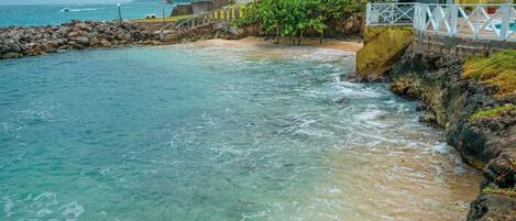 A coastal hotel with a beach view, a rocky shoreline, and a white fence.
