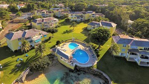Ein Resort mit mehreren gelben Gebäuden, einem zentralen Schwimmbad und dichter umliegender Bepflanzung.