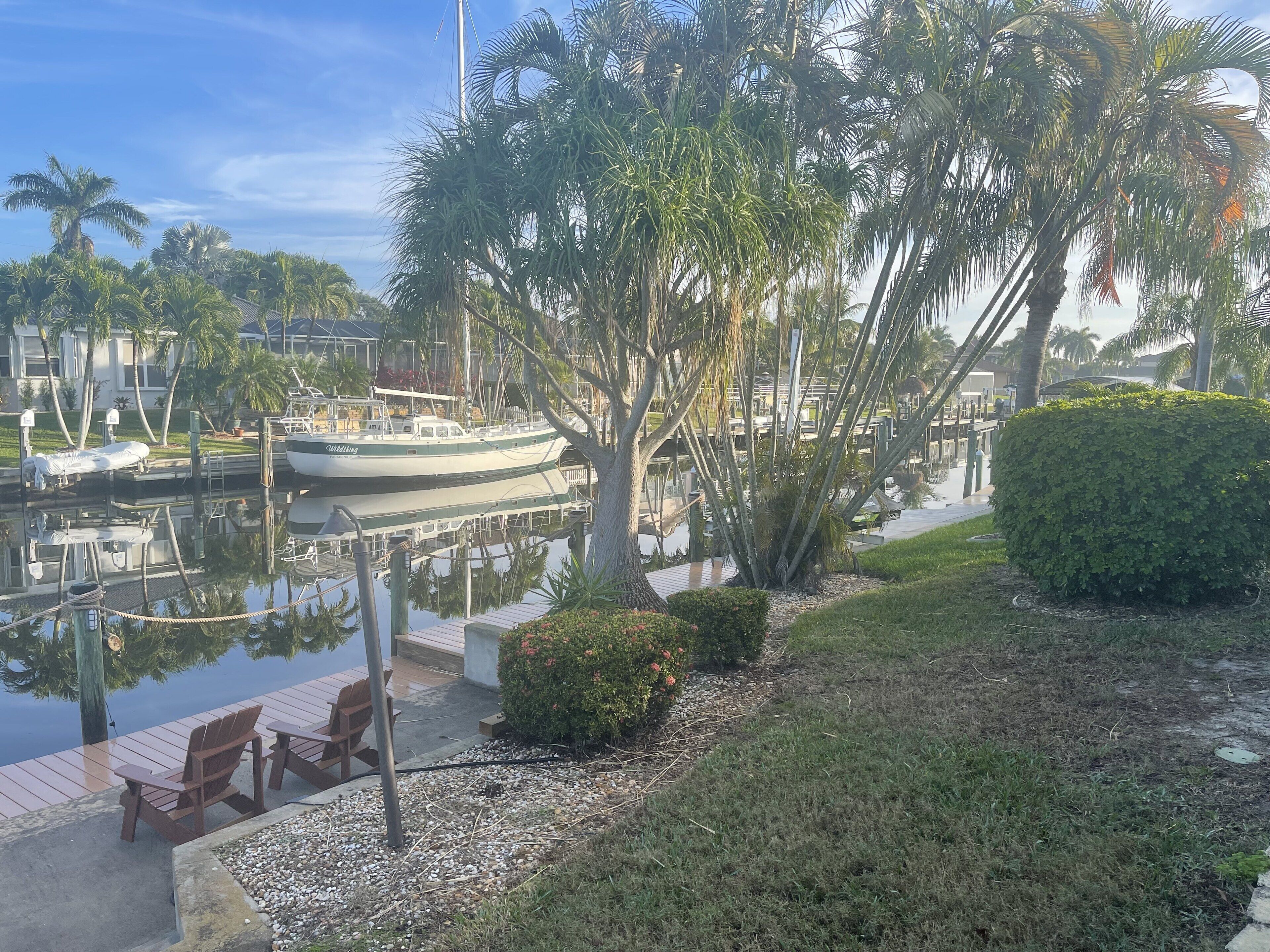 Un puerto deportivo con barcos amarrados, rodeado de palmeras y un área verde con un banco.