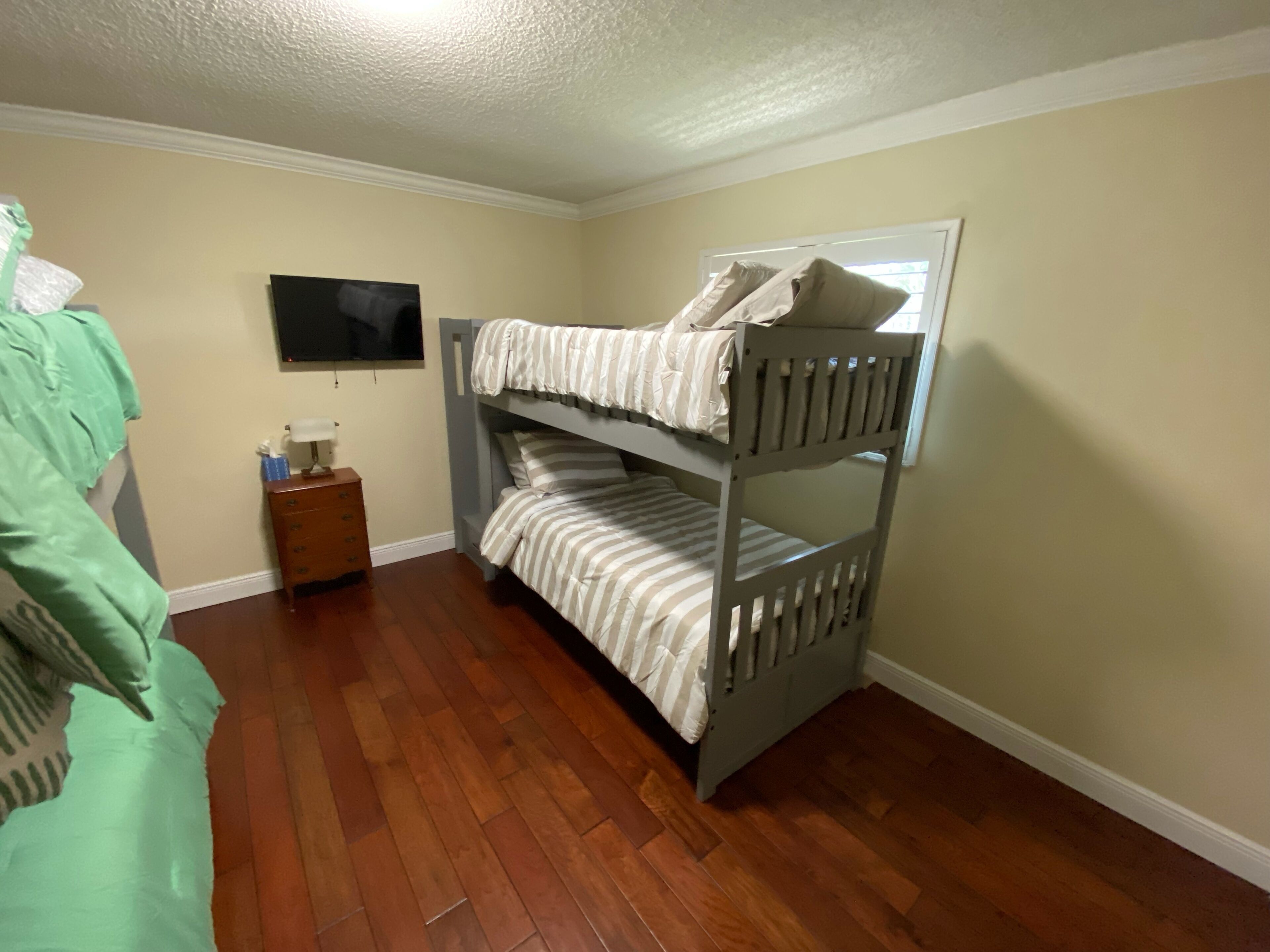 A bunk bed room with a wooden floor, a nightstand, and a television on the wall.