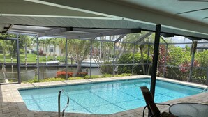 A covered outdoor swimming pool with a view of a canal and greenery. - Dream Vacation Pool Home! On the Water! (Cape Coral)