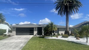 A single-story house with a garage, a well-maintained lawn, and a palm tree. - Dream Vacation Pool Home! On the Water! (Cape Coral)