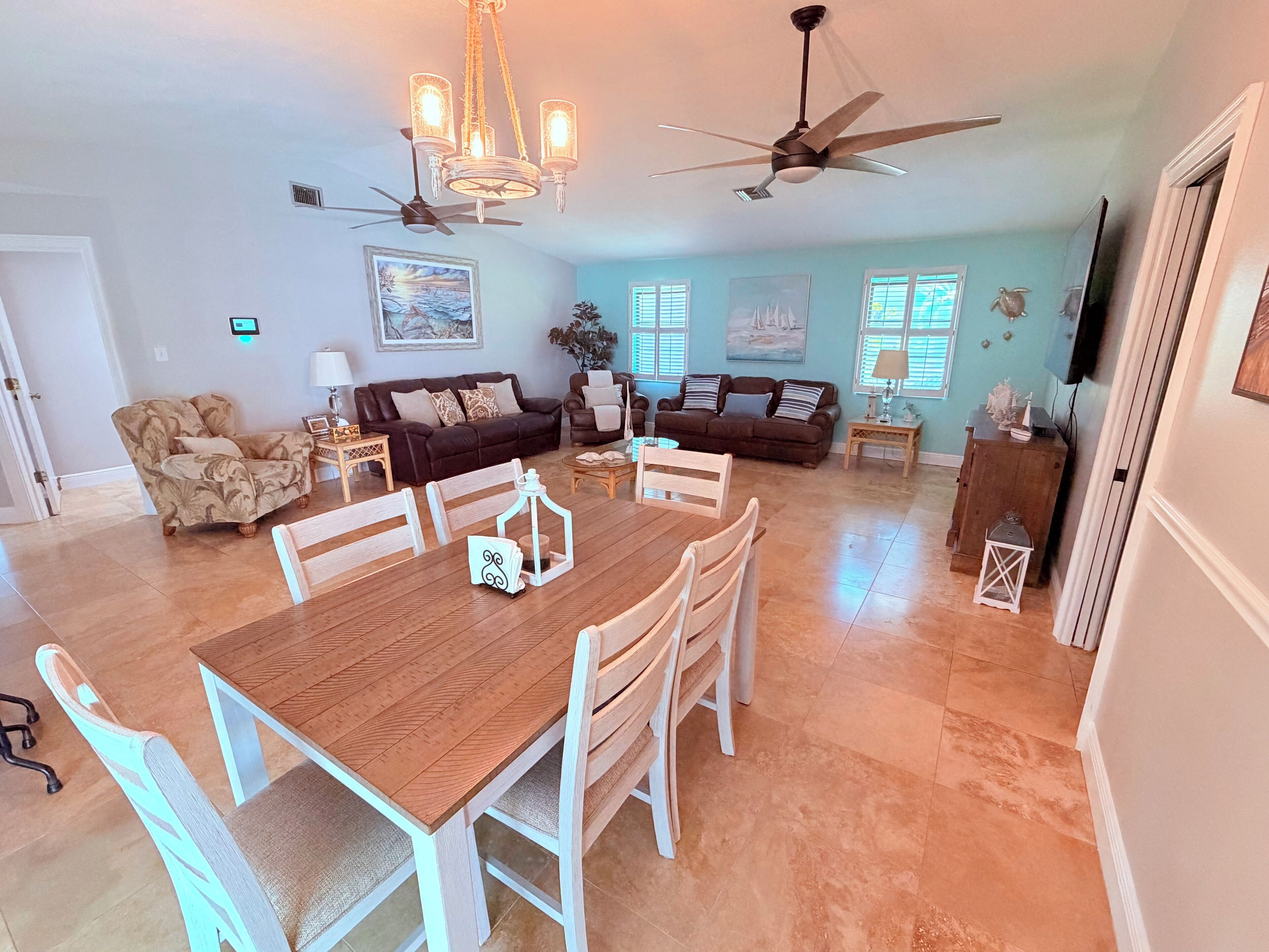 A spacious living room with a dining area, a ceiling fan, and a TV mounted on the wall.