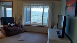 Un salón con vistas al mar a través de un ventanal amplio, un sofá, un escritorio con una computadora y una lámpara.