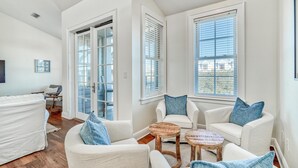 Un salon spacieux doté d’une grande porte-fenêtre coulissante donnant sur un balcon, de meubles blancs et offrant une vue sur l’extérieur.